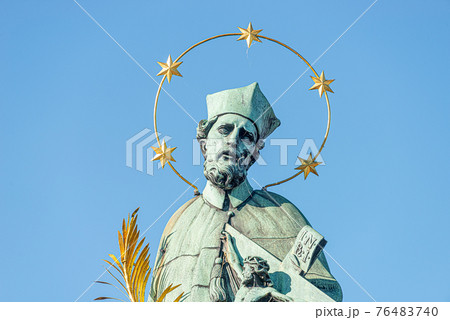 Statue of saint with cross at the Charles Bridge in Prague at blue gradient sky, Czech Republic, summer time Statue of saint with cross at the Charles Bridge in Prague at blue gradient sky, Czech Republic, summer time 76483740