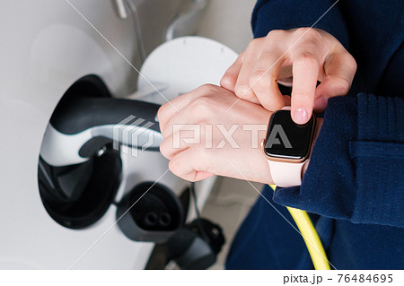 Woman uses her smart watch for opening an electric car and unplugging EV. Disconnecting the plug from charging the electric vehicle Woman uses her smart watch for opening an electric car and unplugging EV. Disconnecting the plug from charging the electric vehicle 76484695