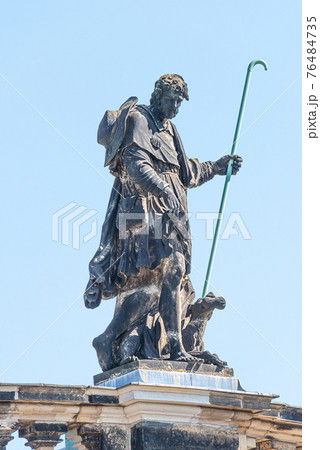 Old roof church statute of a pilgrim with stick and dog in historical downtown of Dresden, Germany, details, closeup. Old roof church statute of a pilgrim with stick and dog in historical downtown of Dresden, Germany, details, closeup. 76484735