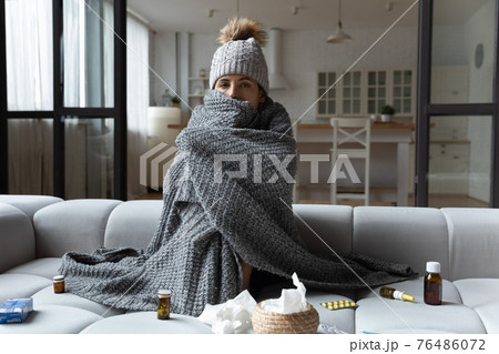 Sick woman sitting in cap covered with plaid taking medicine Sick woman sitting in cap covered with plaid taking medicine 76486072