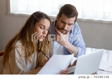 Pensive couple pay online on laptop considering paperwork 76486146