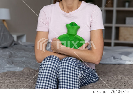 Woman sit on bed hold hot water bottle on belly 76486315