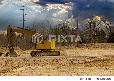 Construction of new road in a excavator digs the ground the view under construction road place Construction of new road in a excavator digs the ground the view under construction road place 76486560