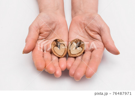 The woman's hands hold two halves of walnut in the form of a heart on a white background, isolated The woman's hands hold two halves of walnut in the form of a heart on a white background, isolated 76487971