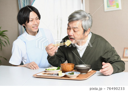 食事をする高齢者男性とエプロン姿の男性介護士 76490233