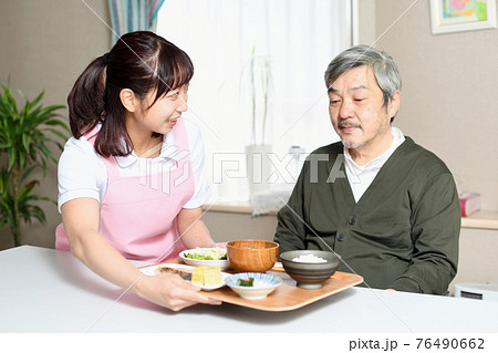 食事を運ぶ女性介護士と高齢者の白髪男性 76490662