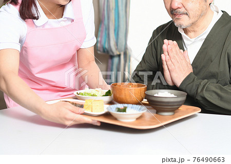 食事を運ぶ女性介護士と高齢者の白髪男性 76490663