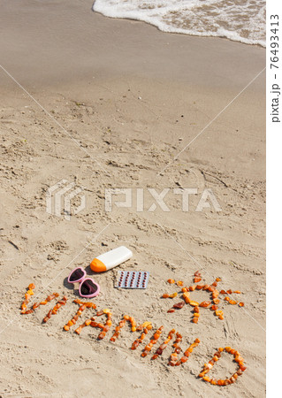 Medical pills, inscription vitamin D and accessories for sunbathing on sand at beach 76493413