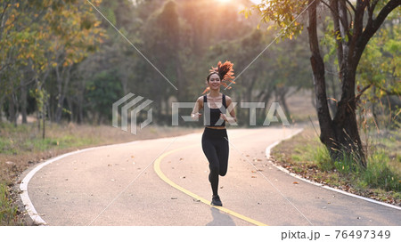 Young sporty woman running in the evening with sunset at the park. 76497349
