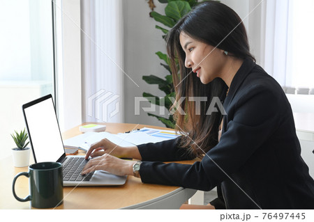 Side view of confident businesswoman working with laptop computer in modern office room. 76497445