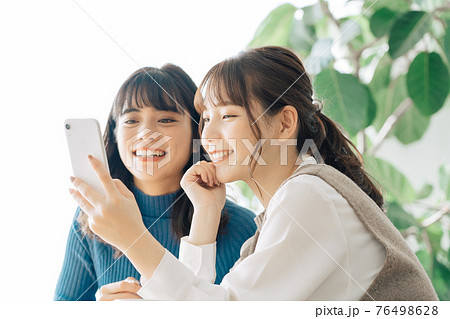 カフェでスマホを見る笑顔の女性2人組 76498628