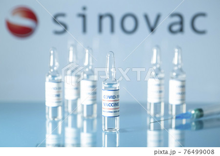 Sinovac vaccine against COVID-19. Glass medical vials with liquid on the background Sinovac company logo. Ampoules with coronavirus vaccine on a medical glass table 76499008