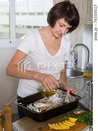 Woman with dorado fish in baking tray 76500017