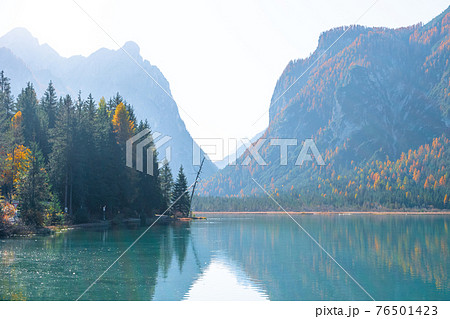 Panoramic view over the Toblacher Lake (Lago di Dobbiaco) and Dolomite mountain summits nearby in Autumn October colors at foggy morning, Dolomites, South Tyrol, Italy 76501423