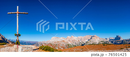 Panoramic view over magical Three Dolomite peaks at the national park Three Peaks (Tre Cime, Drei Zinnen) and a summit cross in Autumn October colors at blue sky, South Tyrol, Italy 76501425