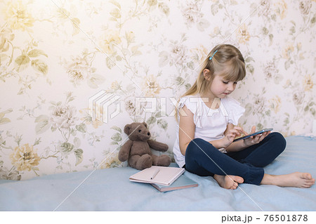 Girl sits on bed, holding phone and reads something in smartphone 76501878