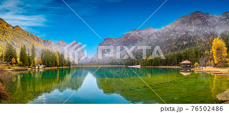 Panoramic view over the Toblacher Lake (Lago di Dobbiaco) and Dolomite mountain summits nearby in Autumn October colors at foggy morning, Dolomites, South Tyrol, Italy 76502486