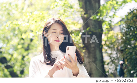 新緑の街でスマホを使う女性 76502852