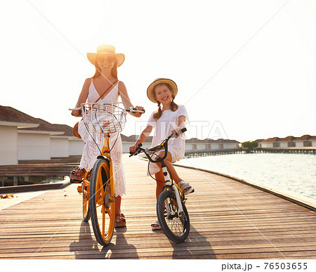 Happy mother and daughter riding bikes on pier Happy mother and daughter riding bikes on pier 76503655