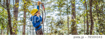 BANNER, LONG FORMAT Happy child in a helmet, healthy teenager school boy enjoying activity in a climbing adventure park on a summer day 76504343