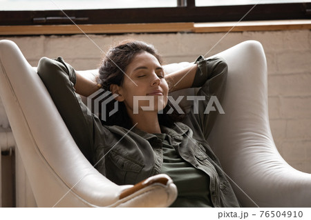 Close up relaxed woman with closed eyes sitting in armchair 76504910