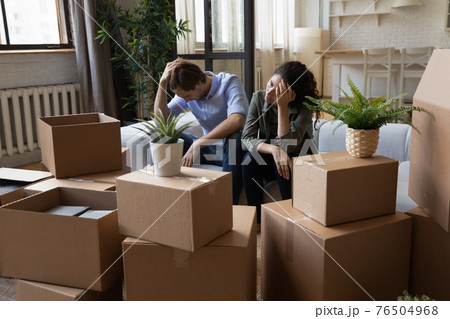 Unhappy frustrated couple sitting on couch with cardboard boxes, eviction 76504968