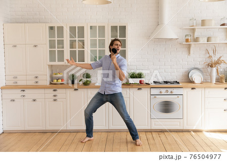 Funny man singing into kitchenware, dancing, having fun in kitchen 76504977