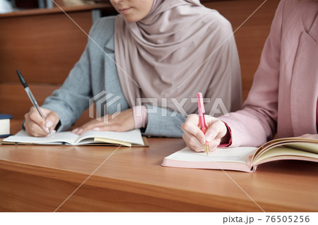Hands of two young female students with pens making notes in copybooks at lecture Hands of two young female students with pens making notes in copybooks at lecture 76505256