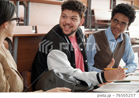Happy guy with pencil looking at groupmate during discussion of project topic or passage from book Happy guy with pencil looking at groupmate during discussion of project topic or passage from book 76505257