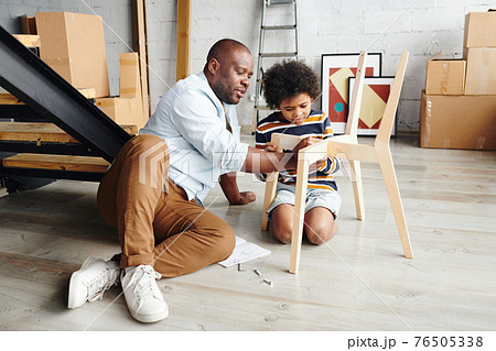 Young father teaching his cute little son how to assemble wooden chair while fixing its parts 76505338