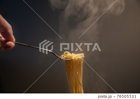 Traditional Italian hot spaghetti hanging from the fork hold by hand with vapor around. Traditional Italian hot spaghetti hanging from the fork hold by hand with vapor around. 76505531