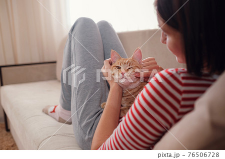 woman relaxing with her ginger pet on a sofa. Cosy scene, hygge concept. 76506728