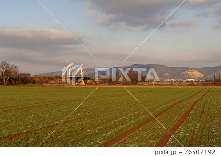 Field of crops at early spring with view of a bridge and hills during golden sunset near Heidelberg, Germany, reddish sundown Field of crops at early spring with view of a bridge and hills during golden sunset near Heidelberg, Germany, reddish sundown 76507192