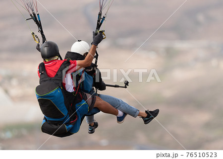 Flying tandem paragliders over the city on a sunny day 76510523