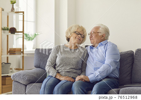 Happy loving senior couple hugging and looking at each other while sitting on sofa at home. 76512968
