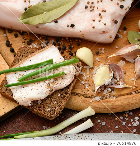 raw pork meat and lard with salt, spices and garlic on a cutting board, dark wooden background 76514976