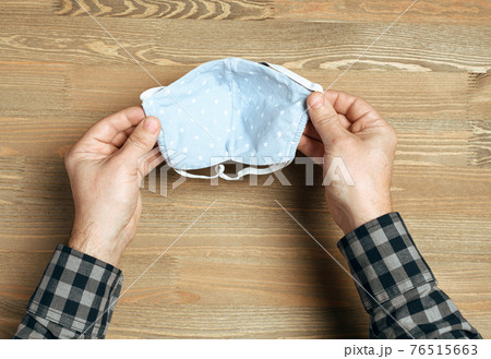 hands with handmade breathing mask on a wooden background, checkered shirt in rustic style, health care prevention of coronavirus infection, as well as other viruses and pollution 76515663