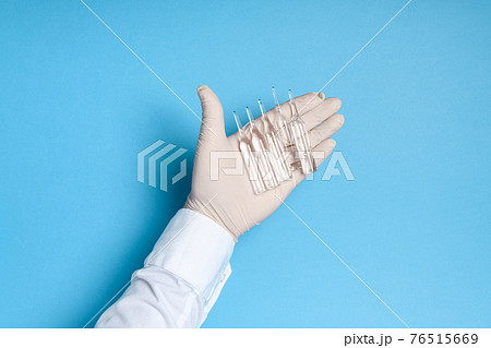hands in medical gloves with ampoules of medicine or vaccine, blue background, imitation of a coronavirus vaccine, prevention of infection with viruses and bacteria 76515669