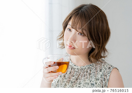 窓辺で紅茶のカップを持つ若い女性 76516015
