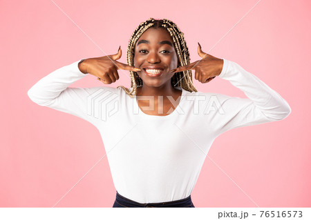 African american woman pointing forefingers at mouth and teeth African american woman pointing forefingers at mouth and teeth 76516573