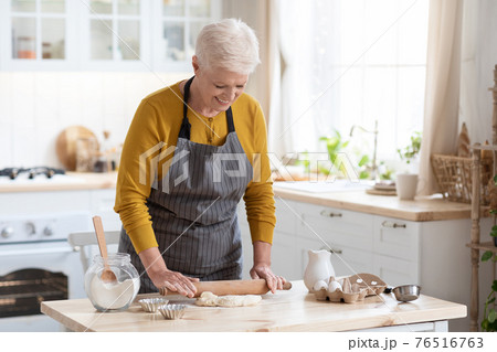Happy grandmother making dough at kitchen, using rolling pin 76516763