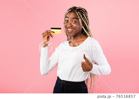 Excited black woman holding credit card showing thumbs up 76516857