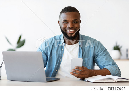 Modern Entrepreneur. Happy Black Man Sitting At Workplace With Smartphone And Laptop Modern Entrepreneur. Happy Black Man Sitting At Workplace With Smartphone And Laptop 76517005