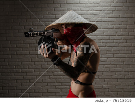 man in an Asian triangular hat with tattoos and a PPSh-41 airsoft gun and against the background of a brick wall man in an Asian triangular hat with tattoos and a PPSh-41 airsoft gun and against the background of a brick wall 76518619