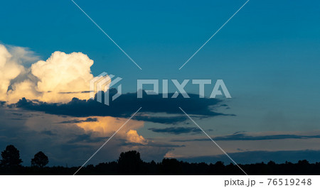 Clouds running across the rapidly darkening sky at sunset. Big cumulus cloud on the evening horizon. The moon goes to the darkened sky Clouds running across the rapidly darkening sky at sunset. Big cumulus cloud on the evening horizon. The moon goes to the darkened sky 76519248