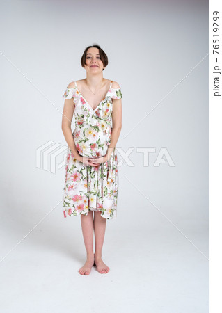 Studio portrait of cheerful young pregnant woman in summer dress on white gray background, happy pregnancy concept 76519299