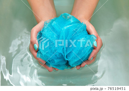 female hands holding a round soft synthetic washcloth in bath with water. Hands close-up. Spa treatment, body care, water background 76519451