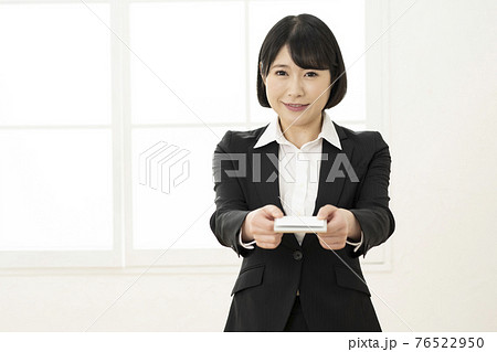 スーツ姿で名刺を差し出す若い女性（正面） 76522950