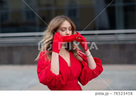 Young woman in red dress and gloves puts on medical facemask 76523458