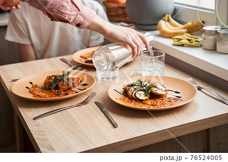 Gay couple enjoying dinner together while drinking water and eating ratatouille 76524005